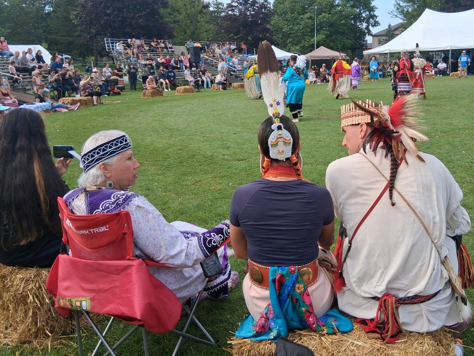 Dancers performing as other participants in regalia watch from the sidelines — Akwesasne International Powwow, Sept. 13, 2026, Lamoureux Park, Cornwall, Ontario, Canada