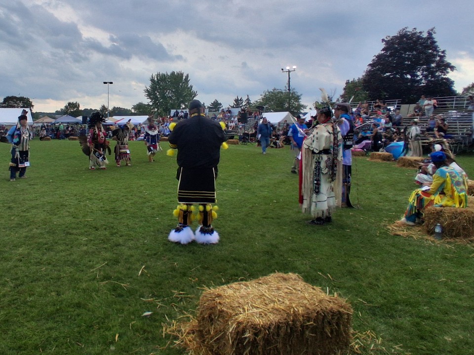 Dancers performing as other participants in regalia watch from the sidelines — Akwesasne International Powwow, Sept. 13, 2026, Lamoureux Park, Cornwall, Ontario, Canada