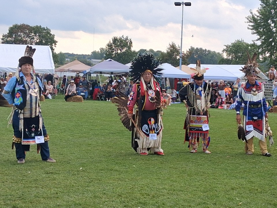 Dancers performing as other participants in regalia watch from the sidelines — Akwesasne International Powwow, Sept. 13, 2026, Lamoureux Park, Cornwall, Ontario, Canada