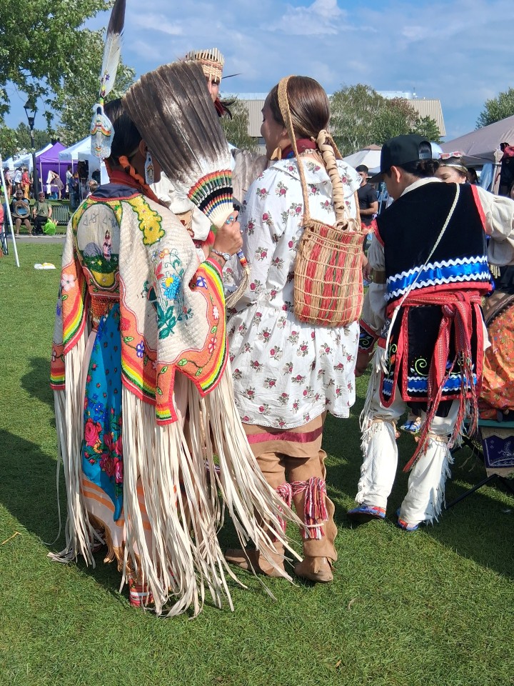 Dancers performing as other participants in regalia watch from the sidelines — Akwesasne International Powwow, Sept. 13, 2026, Lamoureux Park, Cornwall, Ontario, Canada
