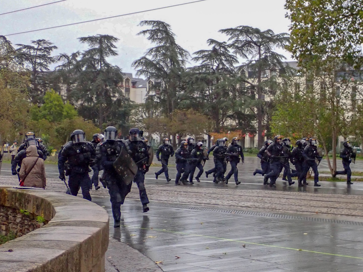 Riot police running across the rain-soaked tram tracks during the protest — Oct. 24, 2026, Nantes, Pays de la Loire, France
