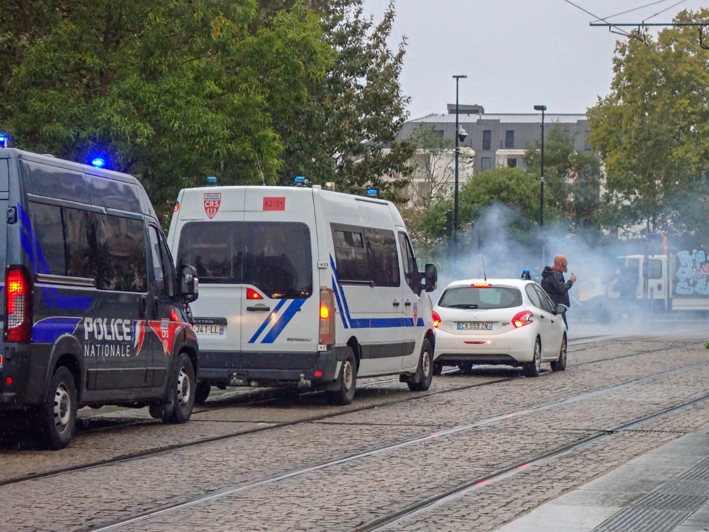 CRS vans on the tram tracks as tear gas spreads across the street — Oct. 24, 2026, Cours John F. Kennedy, Nantes, Pays de la Loire, France